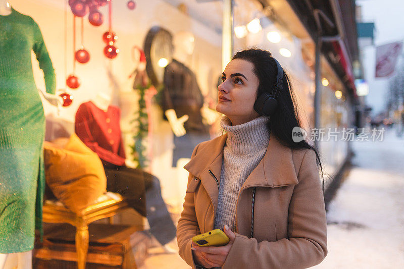 美丽的年轻女子戴着耳机在圣诞节期间逛街