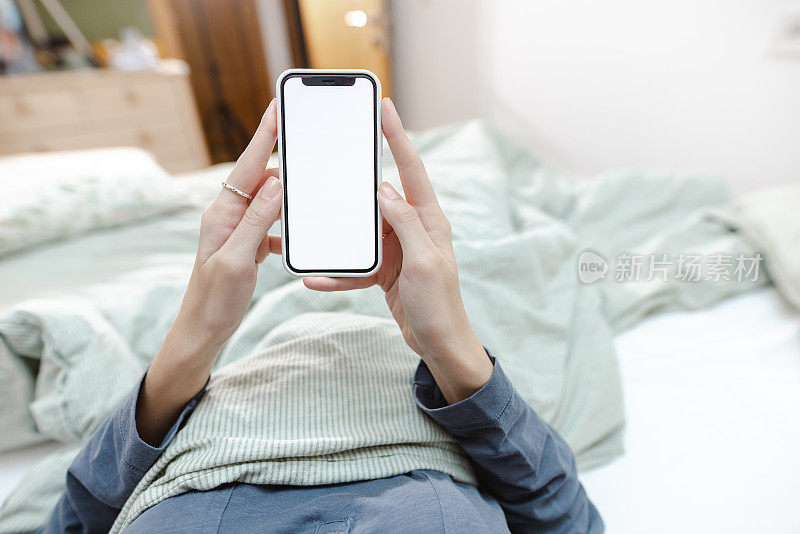 年轻女子在床上拿着白色屏幕的智能手机