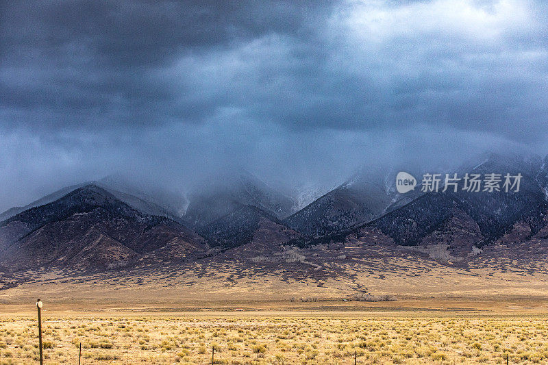 戏剧性的风暴云和雨在平坦的农田和雪山上移动