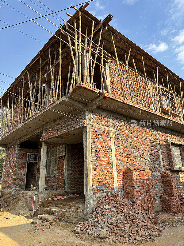 红砖两层楼，厚竹竿支撑胶合板屋顶的建筑特写，住宅区的印度建筑工地，部分建成两层楼，多云，蓝天，重点在前景