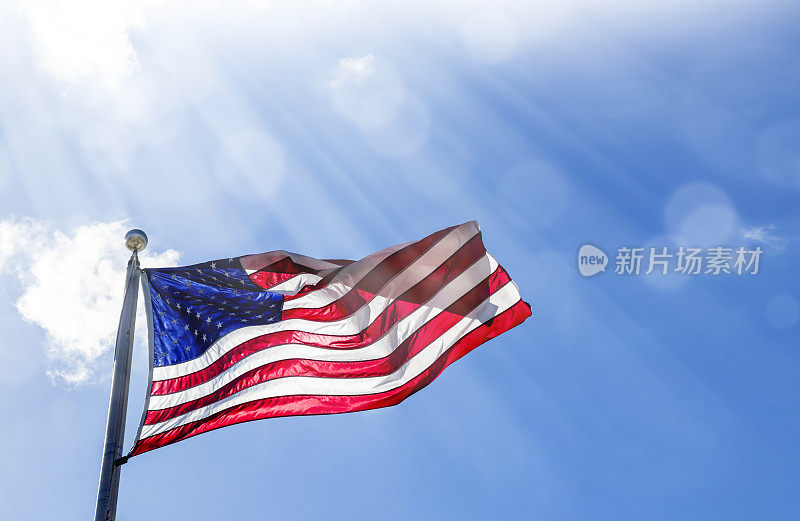 在晴朗的蓝天上，旗杆上飘扬着美国国旗