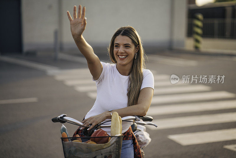 漂亮的年轻女子坐在自行车上向人挥手。