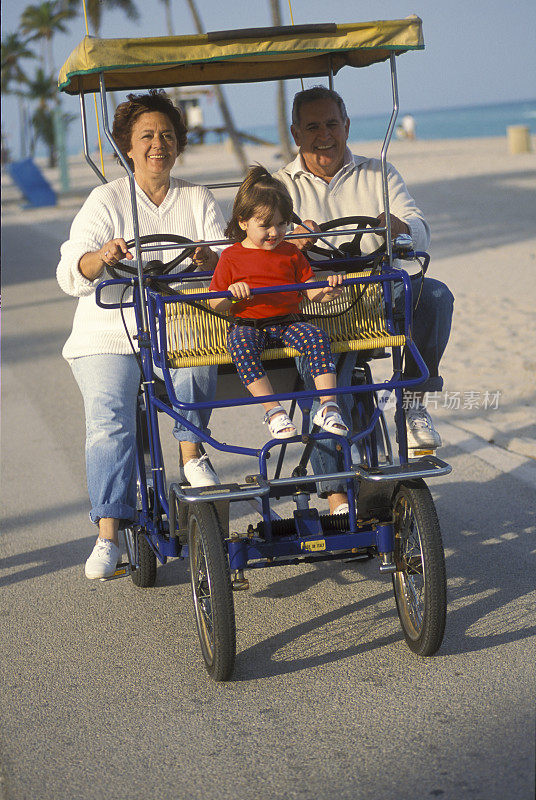 爷爷奶奶和孙女在沙滩上骑着家庭自行车