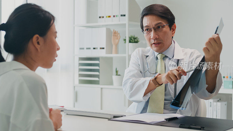 成年亚洲男医生向住院的女病人出示肺部x光检查结果和描述。医疗保健。