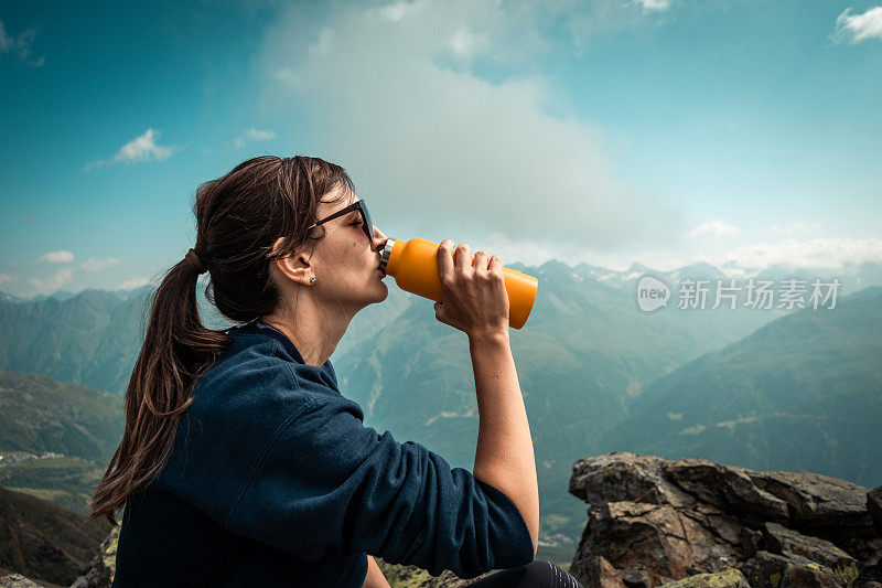 一个徒步旅行者正在用一个黄色的保温瓶喝水。