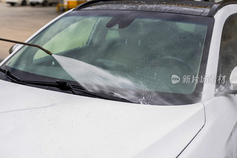 一名男子用加压软管里的水冲洗汽车上的泡沫，这是一家自助洗车店