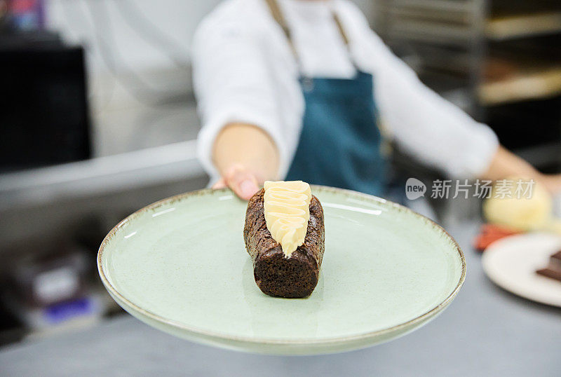 在一家糕点店的厨房里，一位面目全非的糕点师展示了一份奶油巧克力蛋糕的特写。