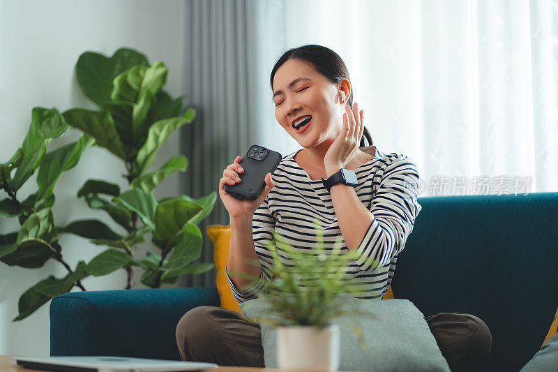 快乐的女人在家里用智能手机和耳机听音乐。