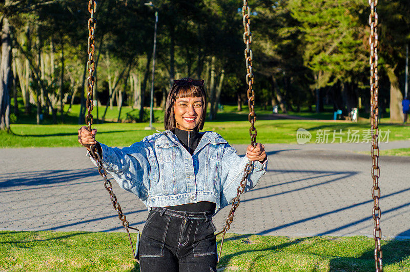 在一个阳光明媚的日子里，一名剪短头发的年轻女子穿着休闲服在公园里荡秋千