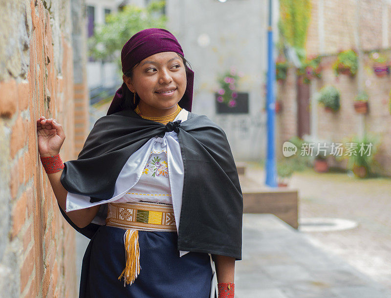 一个微笑的女人靠在砖墙上，她的传统服装为这条古雅而充满活力的小巷增添了一丝优雅。