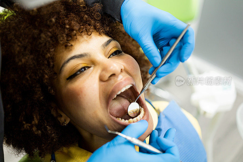 一个有着阿拉伯人容貌的女孩来到牙医诊所。医生用镜子观察留着非洲式发型的黑人女孩的固定牙固位器。牙科家臣。完成正畸治疗。