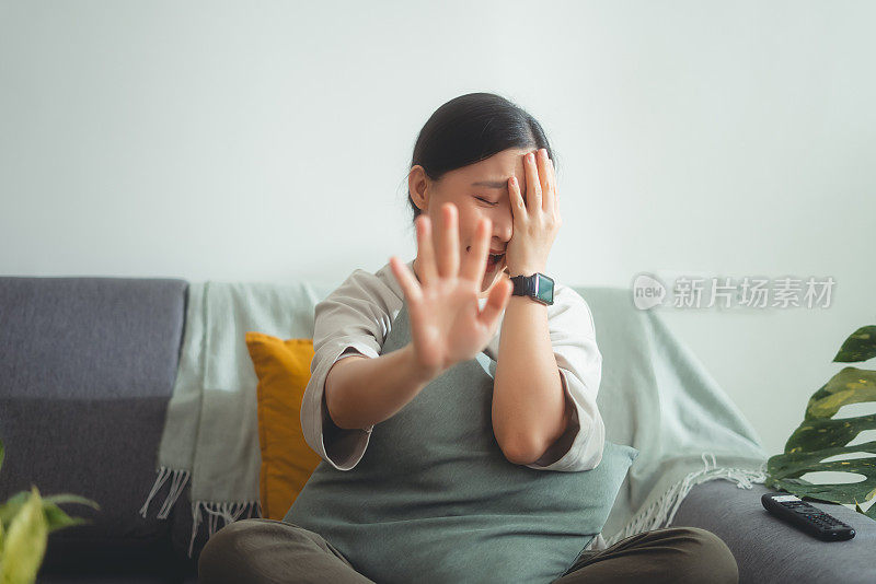 正面看到亚洲女人坐在家里的沙发上看电视，感到害怕。