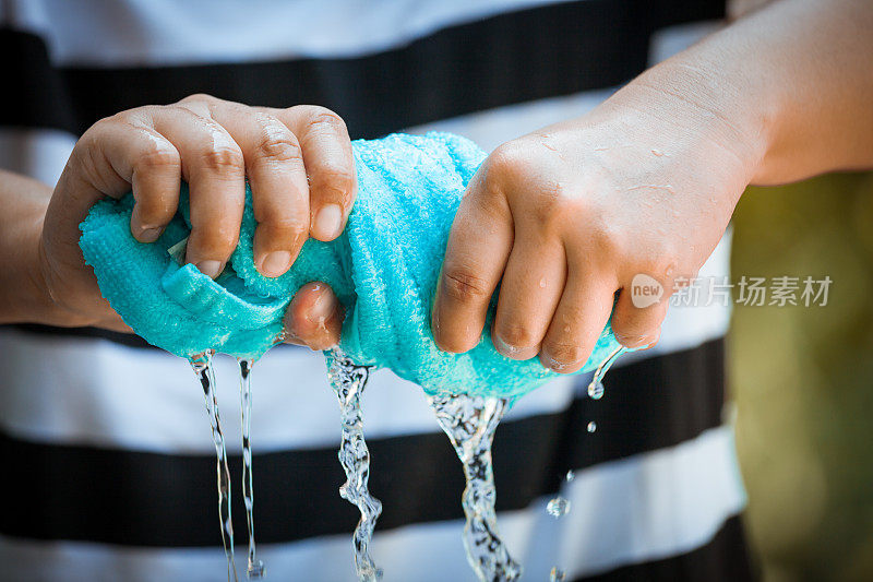 女人双手挤湿了蓝色的毛巾和水滴
