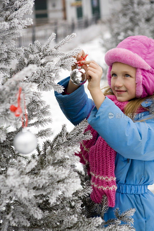 小女孩用圣诞球装饰冰冻的圣诞树。