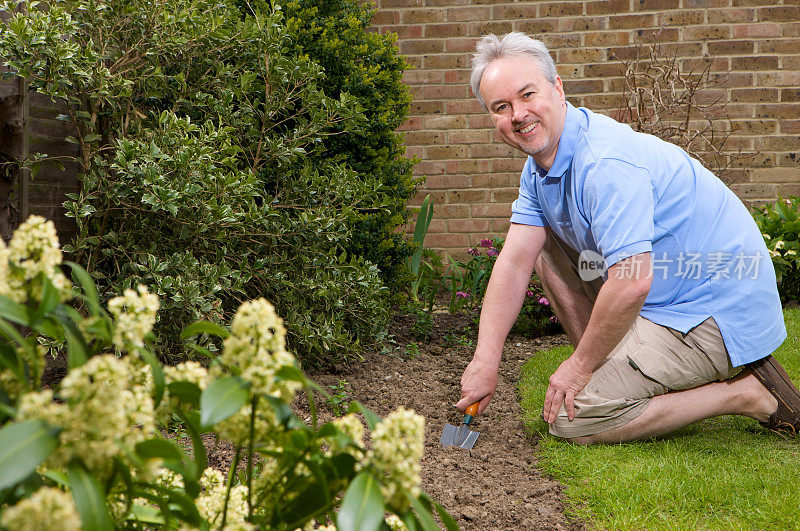 微笑的男人跪着，为他的花园准备土壤