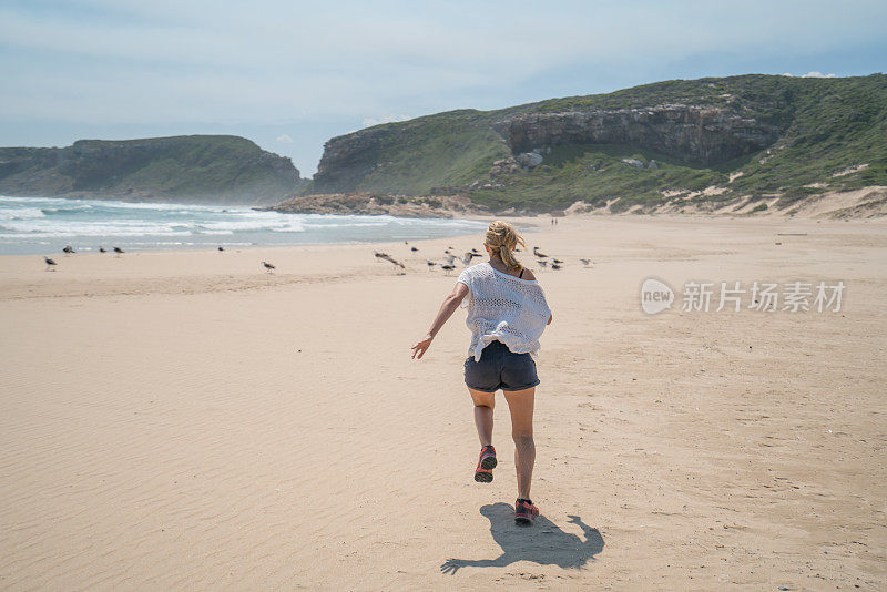 年轻女子在海滩上追逐鸟儿