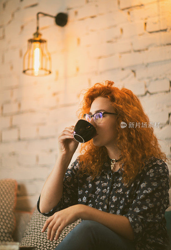 年轻的红头发女人在咖啡馆喝咖啡。