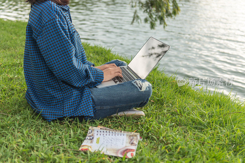 坐在湖边的草地上使用笔记本电脑