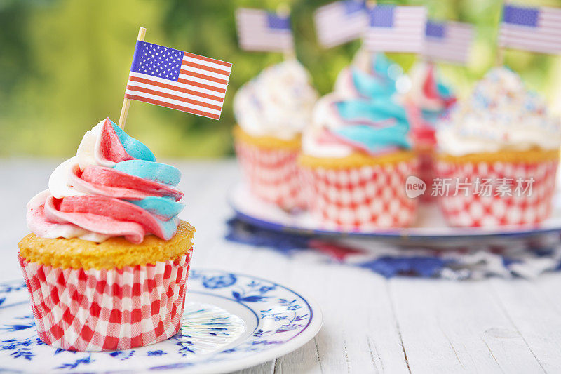 户外桌子上有红白蓝糖霜的纸杯蛋糕和美国国旗