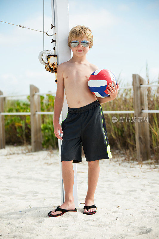 在海滩上，拿着排球的男孩靠在网柱上