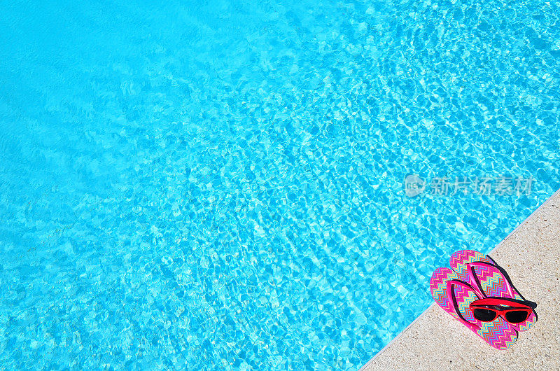 蓝色的泳池旁边是红色的凉鞋和太阳镜