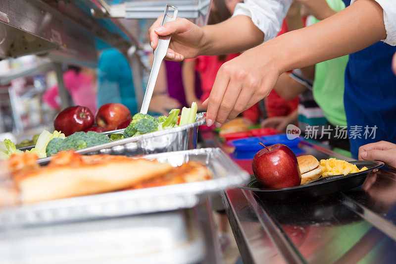 食堂工作人员帮助小学生在午餐排队时选择食物