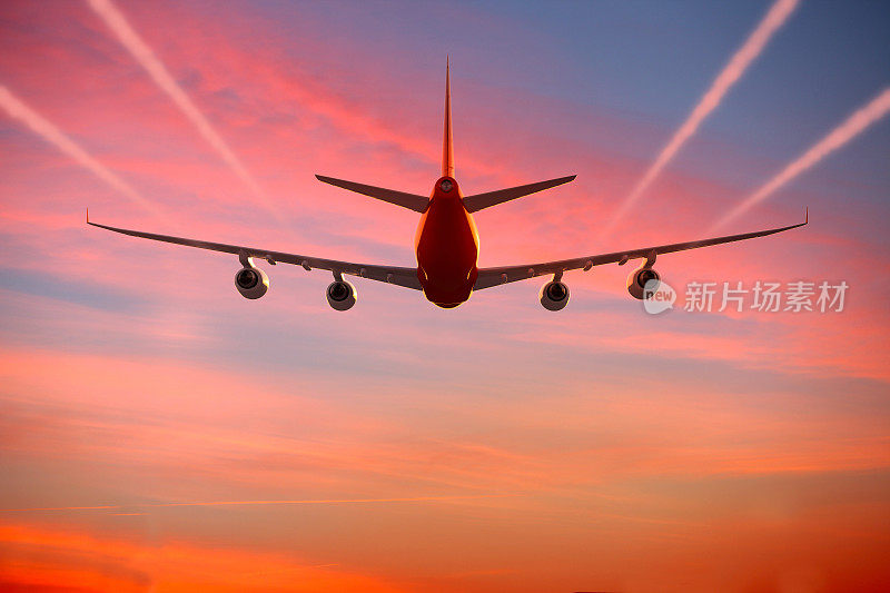 日落时在天空中飞行的飞机带着蒸汽尾迹