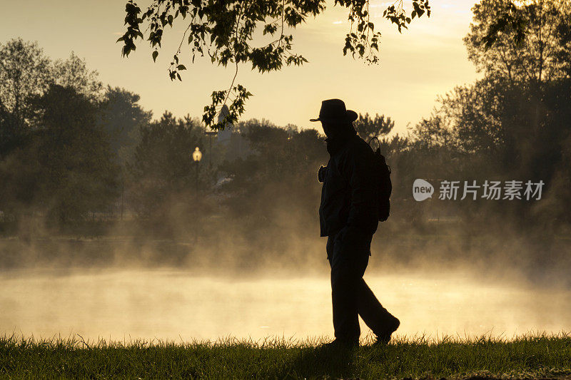 在寒冷的秋天早晨，一个无家可归的人沿着雾蒙蒙的湖走着