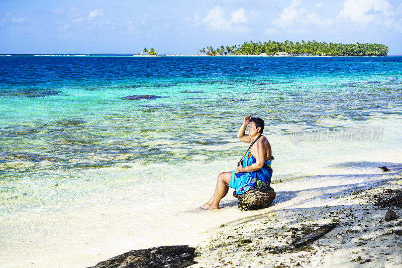 在加勒比海的佩利卡诺岛，一名女子坐在绿松石海附近的岩石上