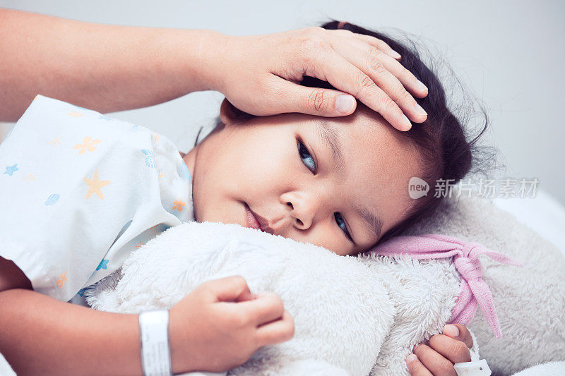 生病的亚洲女孩躺在床上，母亲用手抚摸着她的额头