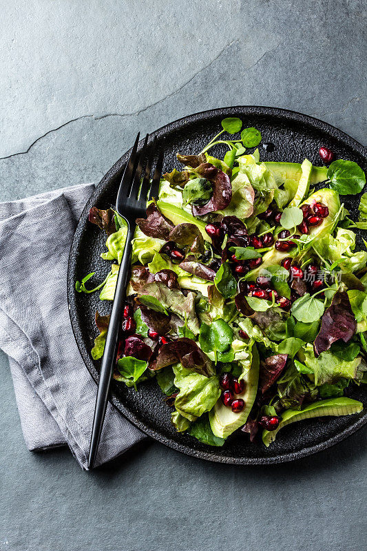 健康的生菜沙拉，豆瓣菜沙拉和石榴在黑色的盘子