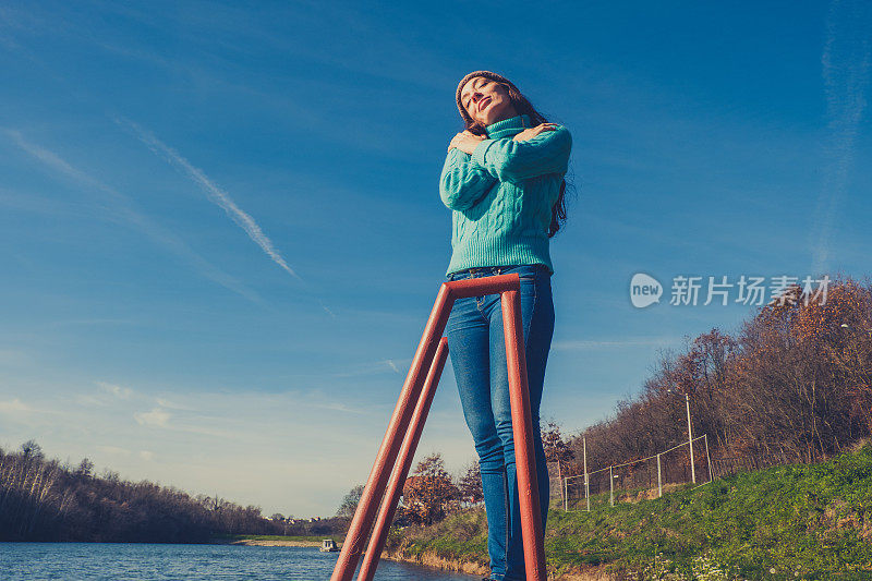 年轻女子躺在湖边的码头上，披着毯子，看日落