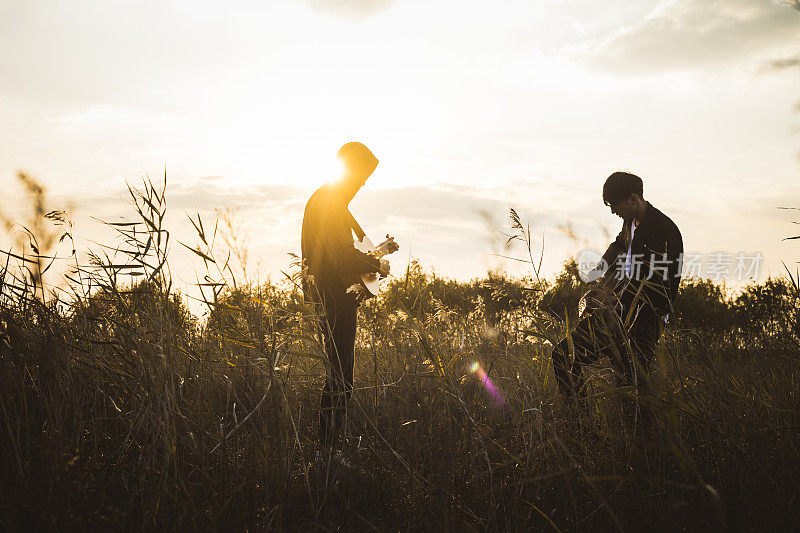 两个男人，朋友在草地上练习原声吉他