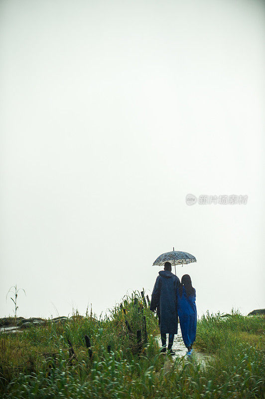 后视图的情侣一起走在雨中雨衣和雨伞