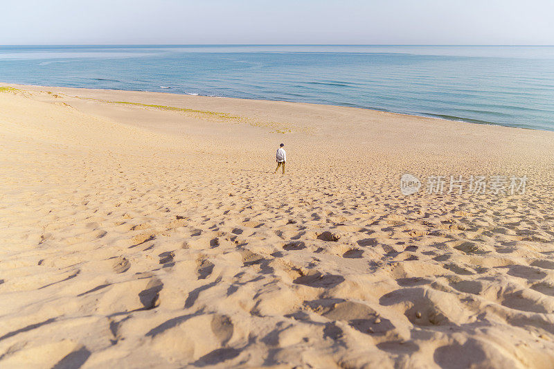 男游客走在沙丘上望着大海