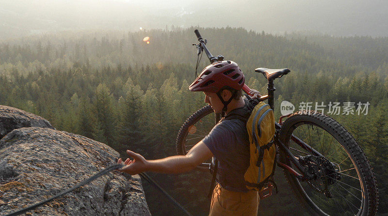 山地自行车手使用绳子爬山，在高山和山谷之上