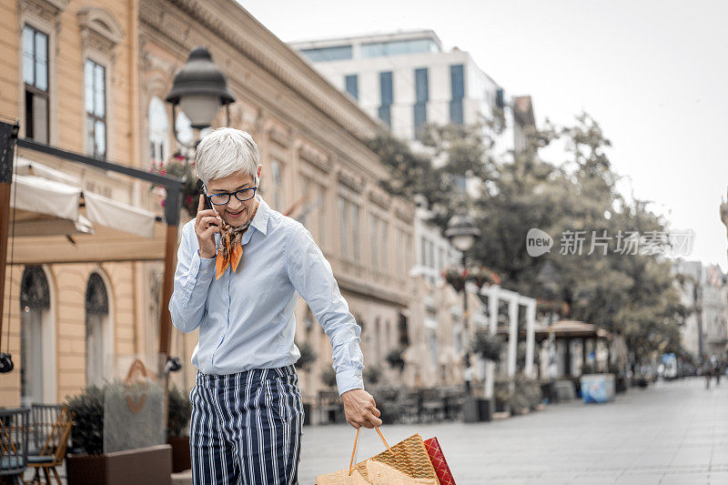 老女人走在城市的街道上，用她的智能手机说话