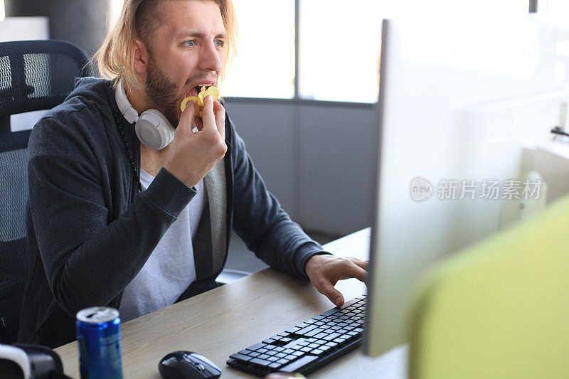 穿着休闲服装的专注的年轻人使用电脑，播放游戏或攻略视频，吃着薯条。