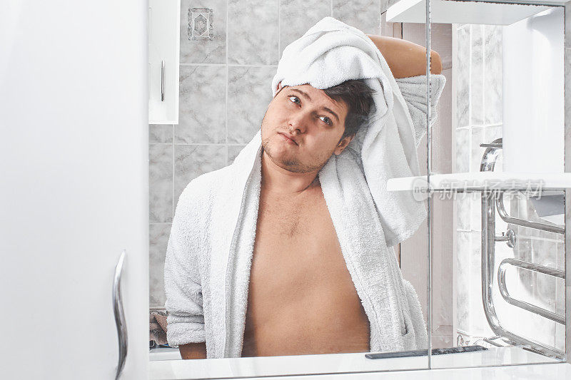 一名穿着白色浴衣的男子在浴室的镜子前用白毛巾擦拭头发。