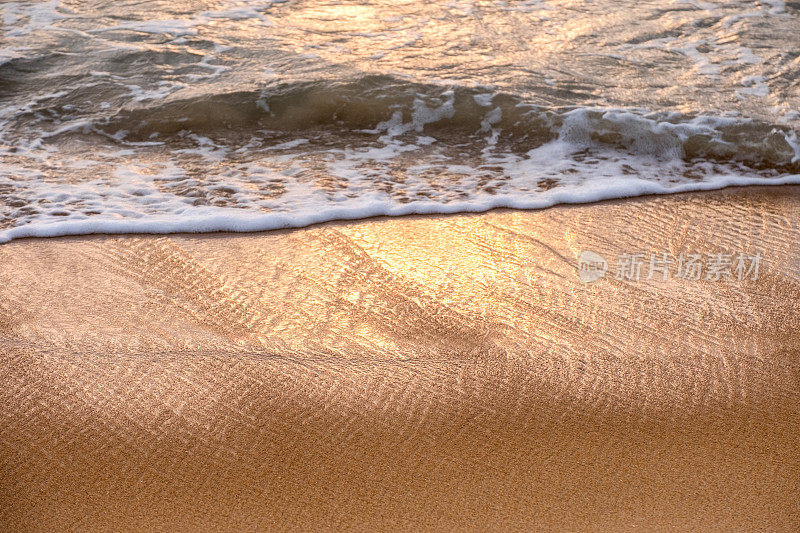 日落时分，棕色海滩上闪闪发光的热带海浪带着泡沫