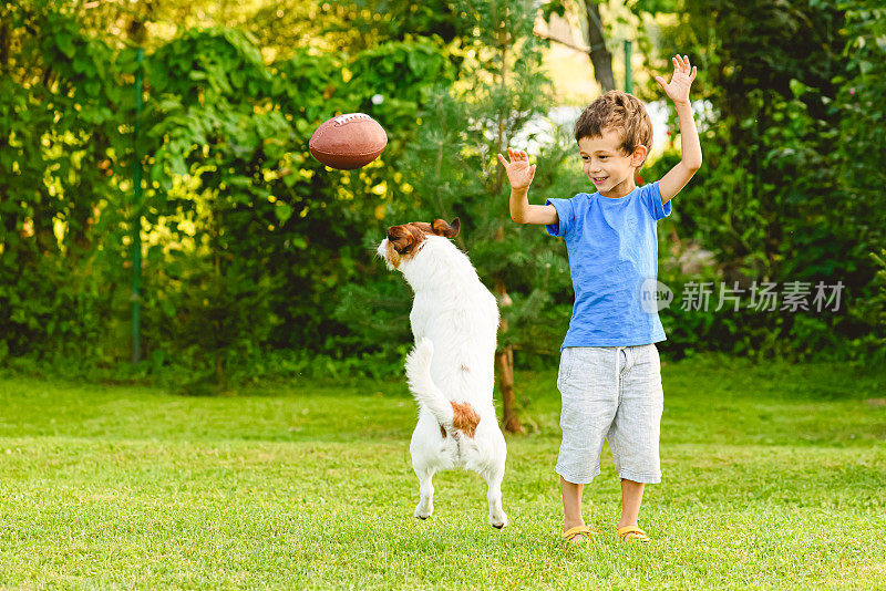 在后院的草坪上和一个小男孩和他的宠物狗玩橄榄球