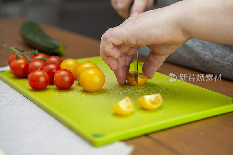 用手在绿色砧板上切一个樱桃番茄