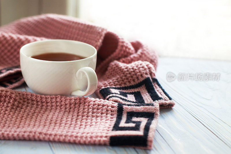 一杯热咖啡和针织毛衣放在靠近窗户的木桌上，冬天的早晨概念