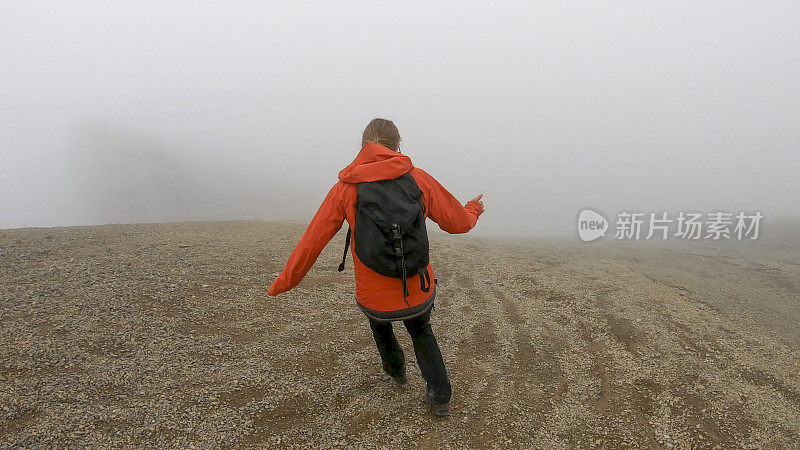 年轻的女登山运动员在雾中爬下一座山