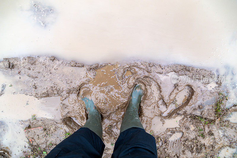 脚在绿色橡胶靴子站在湿漉漉的棕色泥坑直接俯瞰