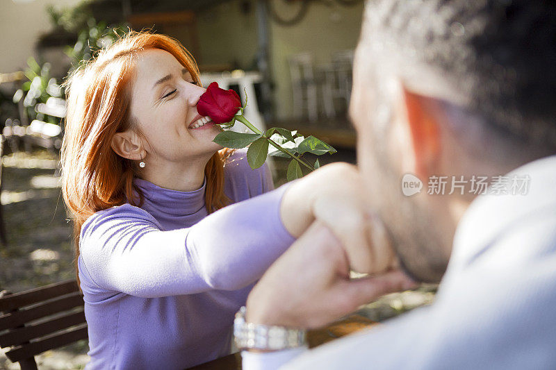 一名男子正在亲吻一位手持鲜花的红发年轻女子的手