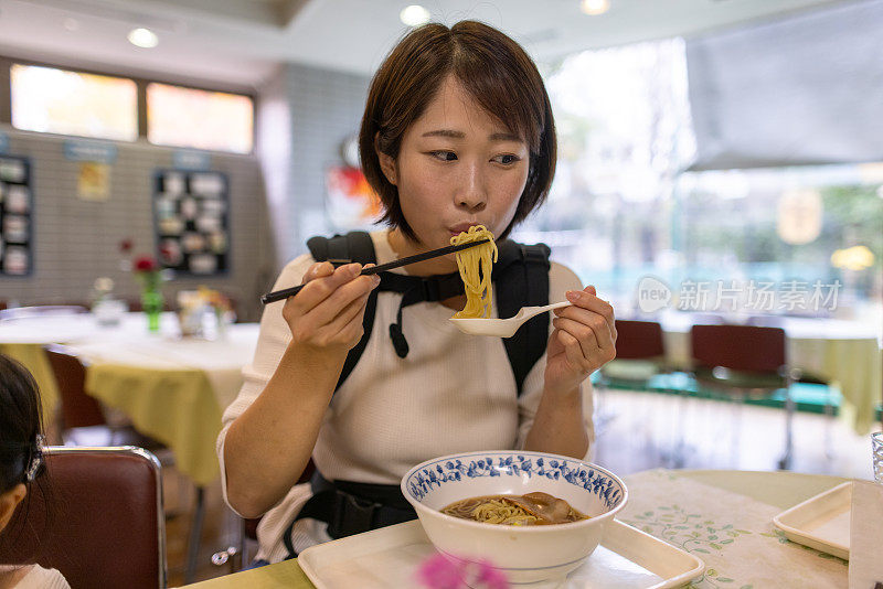 一位年轻的母亲背着她的男婴在餐馆吃拉面