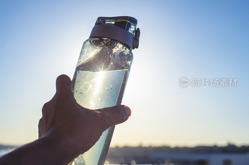 一个人在阳光下举着一个灰色的可重复使用的水瓶。