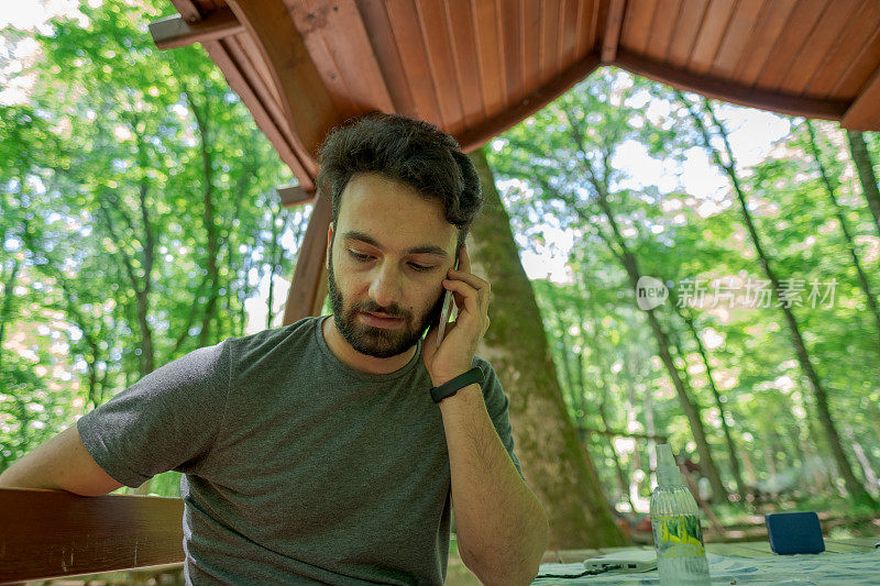 一个英俊的担心焦虑的男人与黑胡子在森林野餐在公共公园概念下打电话