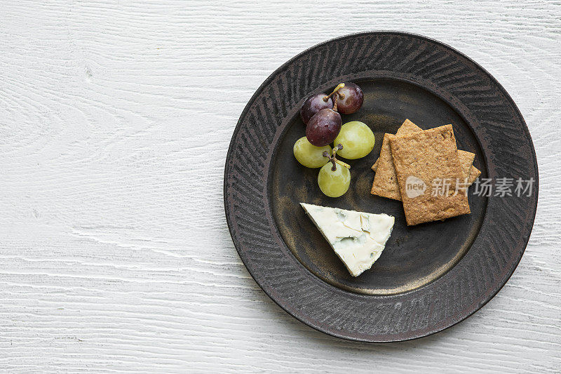 一张白色的木桌上放着四份丹伯特奶酪，还有饼干和葡萄